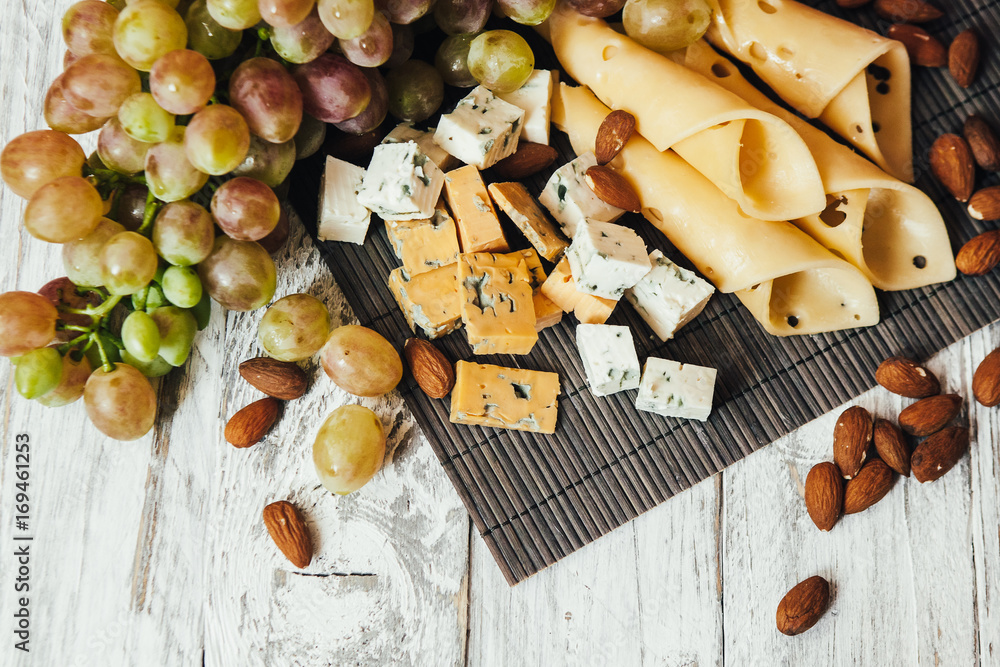 Assortment of cheeses with nuts and grapes on a white wooden background Assortment of cheeses with nuts and grapes on a white wooden background