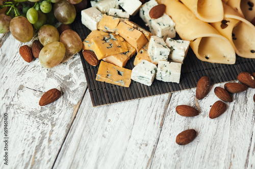 Assortment of cheeses with nuts and grapes on a white wooden background