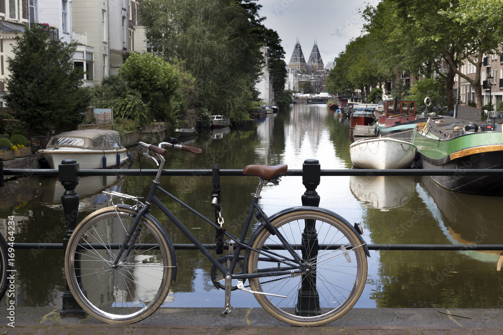 Bicycle at railings and Amsterdam's canal with boats on background