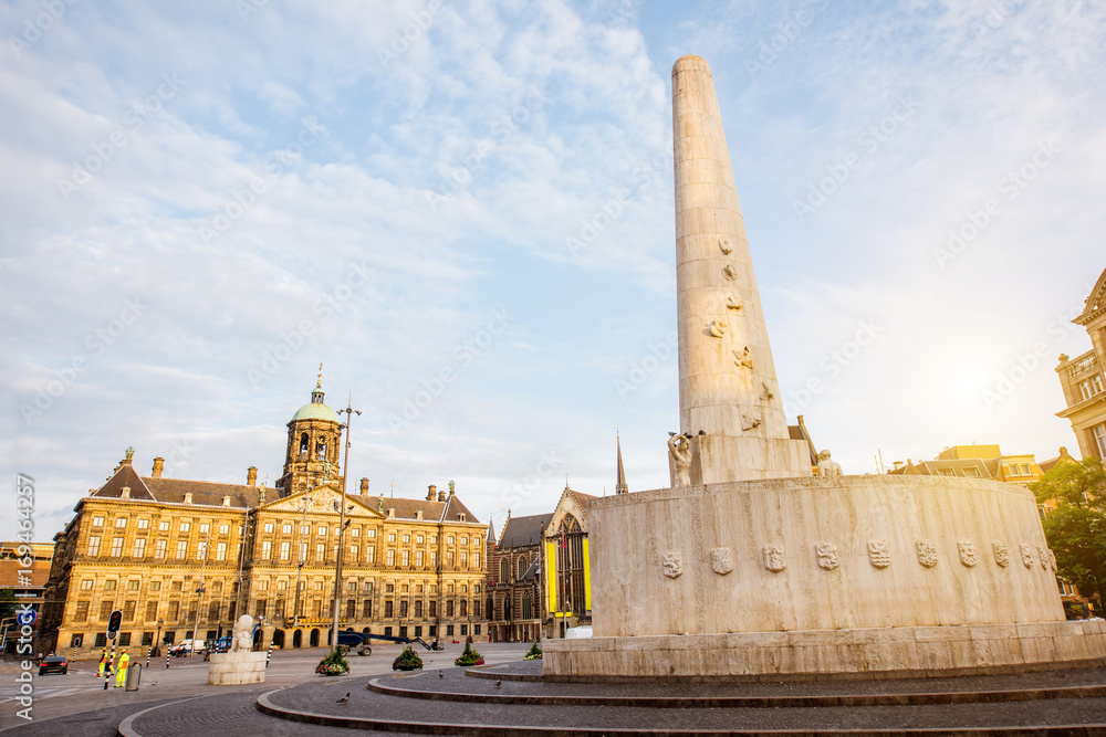 Obraz premium Poranny widok na plac Dam z Pałacem Królewskim i pomnikiem w Amsterdamie podczas słonecznej pogody