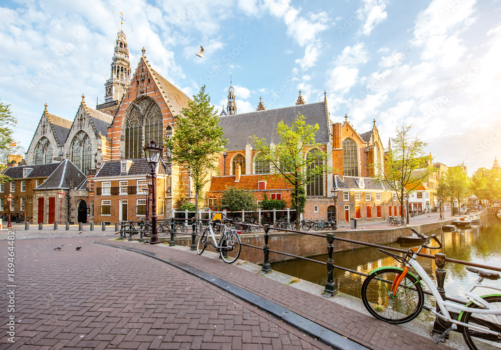 Obraz premium Poranny widok na kanał wodny ze Starym Kościołem podczas słonecznej pogody w mieście Amsterdam