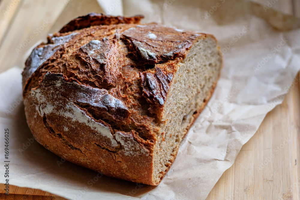 A fresh, crunchy, delicious rye bread on a wrinkled paper and a wooden chopping board
