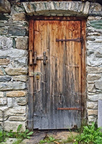 Old wooden door in field stone wall with rusty hinges and padlock
