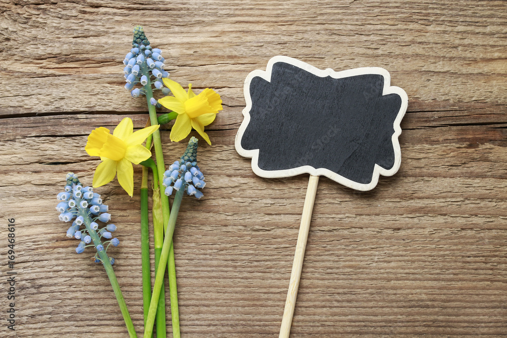 Daffodils, muscari flowers and blank blackboard label on wood Daffodils, muscari flowers and blank blackboard label on wood
