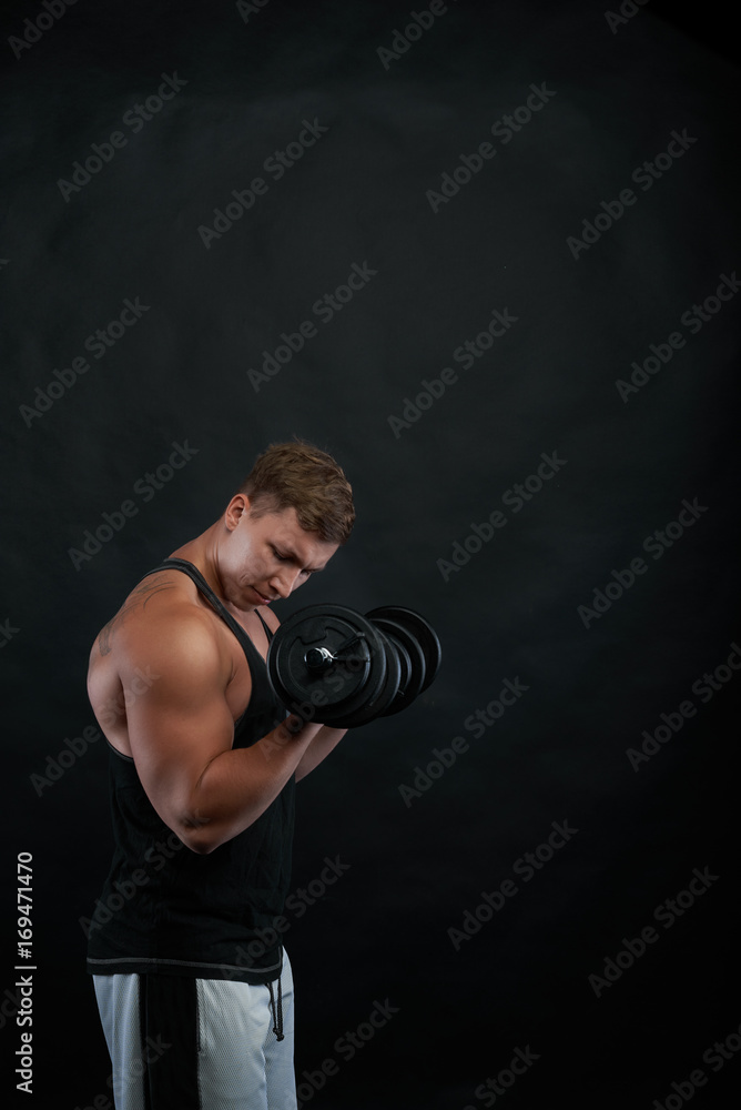 Studio shot of muscular ripped young European bodybuilder dressed in sweatpants and black tank top exercising with dumbbells. Health, fitness, sports, bodybuilding and weightlifting concept