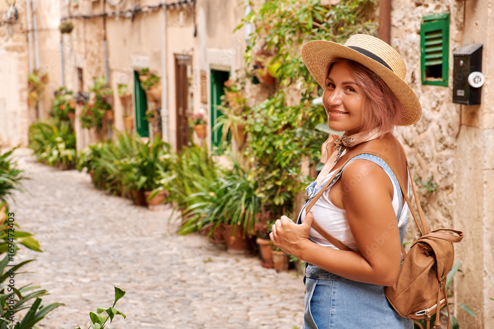 Beautiful pretty woman walking at old town pavement street with flowers and looking away. Travel concept
