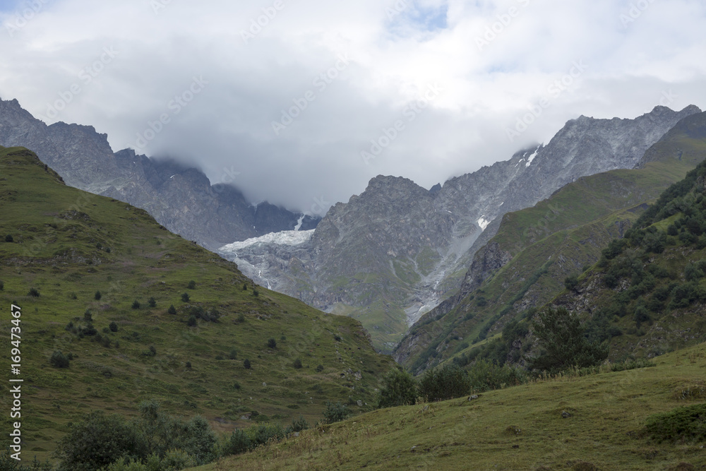 Fototapeta premium Горный пейзаж. Пасмурная погода в живописном ущелье, туман в горах, белые облака. Природа Северного Кавказа