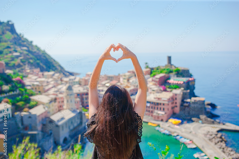 Beautiful girl making with hands heart shape on the old coastal town background of Vernazza, Cinque Terre National Park, Liguria, Italy ,Europe