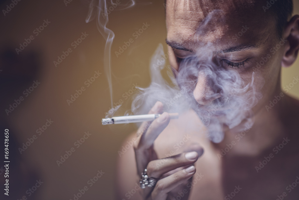 Fototapeta premium Portrait of a young man smoking, letting off a rich cloud of smoke