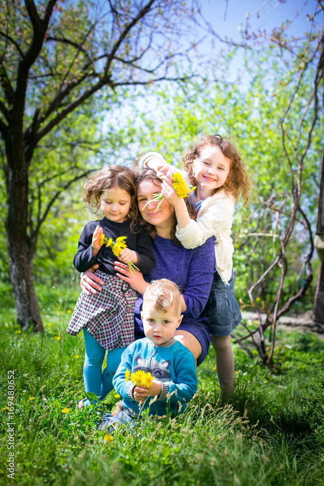 Fototapeta premium Mom with three children - a boy and two girls smiling, and her children are hugging. Happy large family in nature.