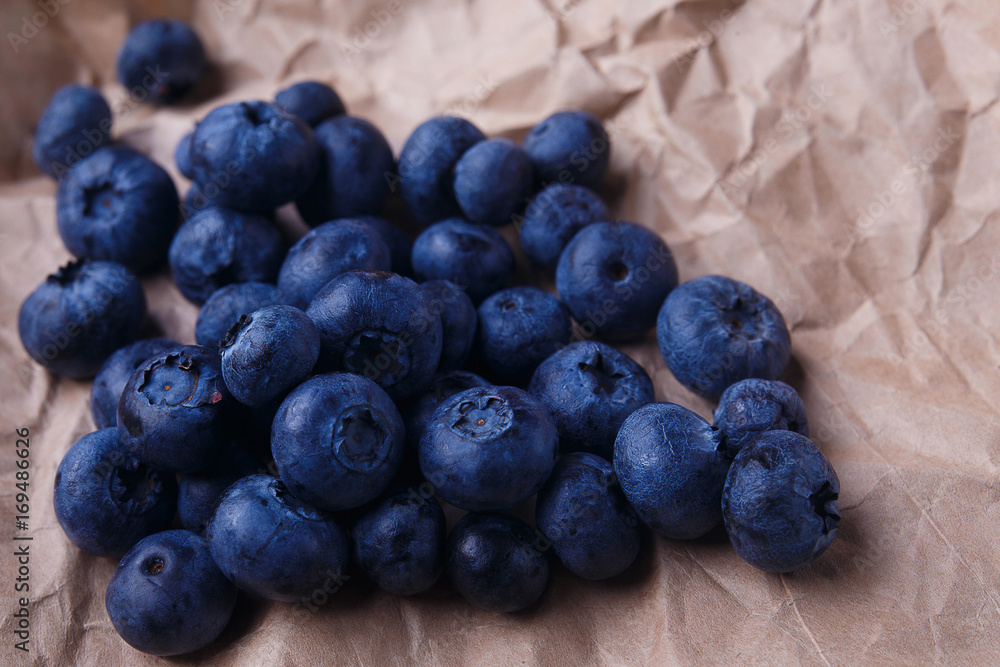 Blueberries on rustic wooden background, close up. Delicious berries on craft paper, macro Blueberries on rustic wooden background, close up. Delicious berries on craft paper, macro