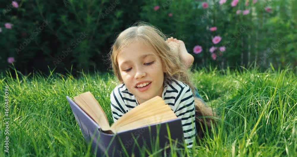 Portrait girl reading book in the grass and smiling at camera Portrait girl reading book in the grass and smiling at camera