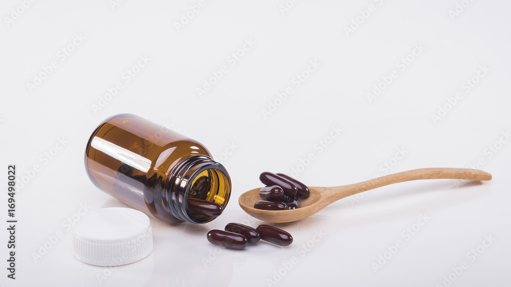 Brown capsules pour out of the bottle and in the spoon , white background. Brown capsules pour out of the bottle and in the spoon , white background.