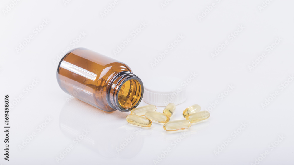 Yellow vitamin capsule is poured from the bottle , white background. Yellow vitamin capsule is poured from the bottle , white background.