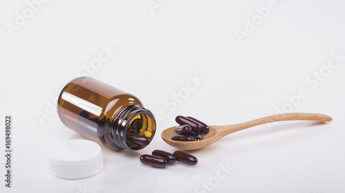 Brown capsules pour out of the bottle and in the spoon , white background.