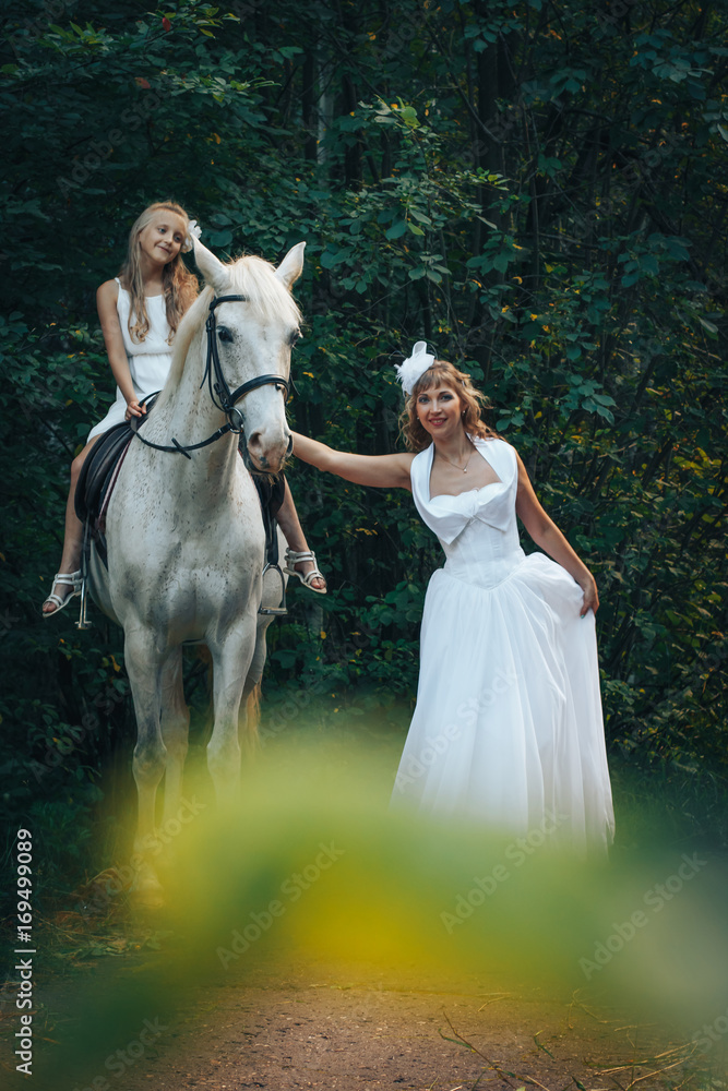 Bride, small girl and white horse in the park