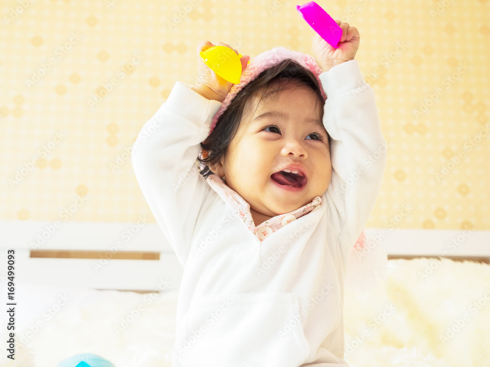 Little baby on white bodysuit holding a colorful toy on hand playing on the bed Little baby on white bodysuit holding a colorful toy on hand playing on the bed