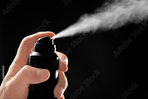 Fotografie Man spraying deodorant on dark background, closeup