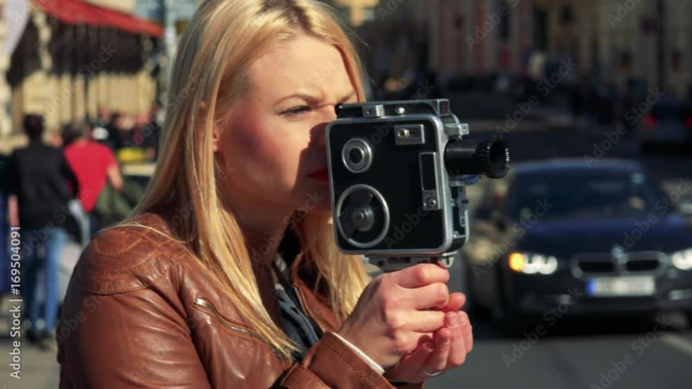 A young attractive woman shoots a video with a camera - closeup - a busy street in the blurry background A young attractive woman shoots a video with a camera - closeup - a busy street in the blurry background