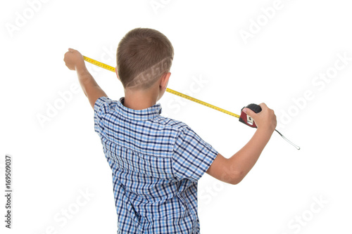 Cute young builder in blue checkered shirt measures something with a measuring tape, isolated on white background