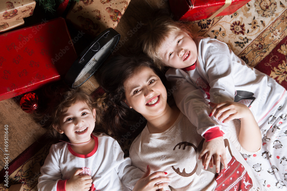 Fototapeta premium Happy family mother and two little daughters having fun lying on a carpet. Winter holiday Xmas and New Year.