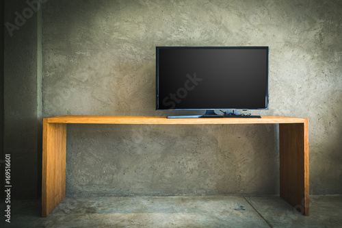 Flat LCD television on wood table in the living room with grunge concrete wall and parquet floor