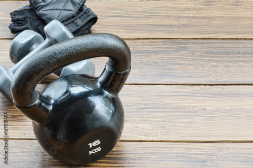 Fototapeta Naklejka Na Ścianę i Meble -  Black kettlebell, grey dumbbells and workout gloves on dark background. Weight lifting  exercise concept. Accessories for gym and fitness. Copy space.