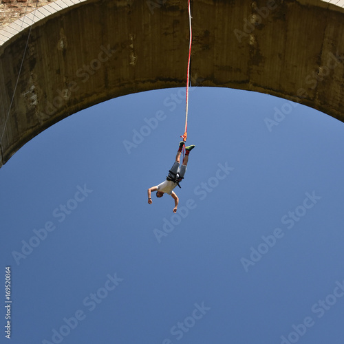 Seen from the ground young man bungee jumper falling down from a high bridge