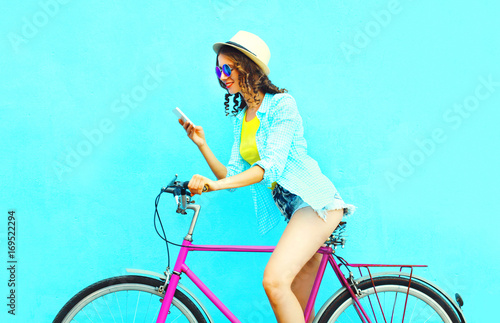 Summer woman using smartphone on retro bicycle on a colorful blue background in profile