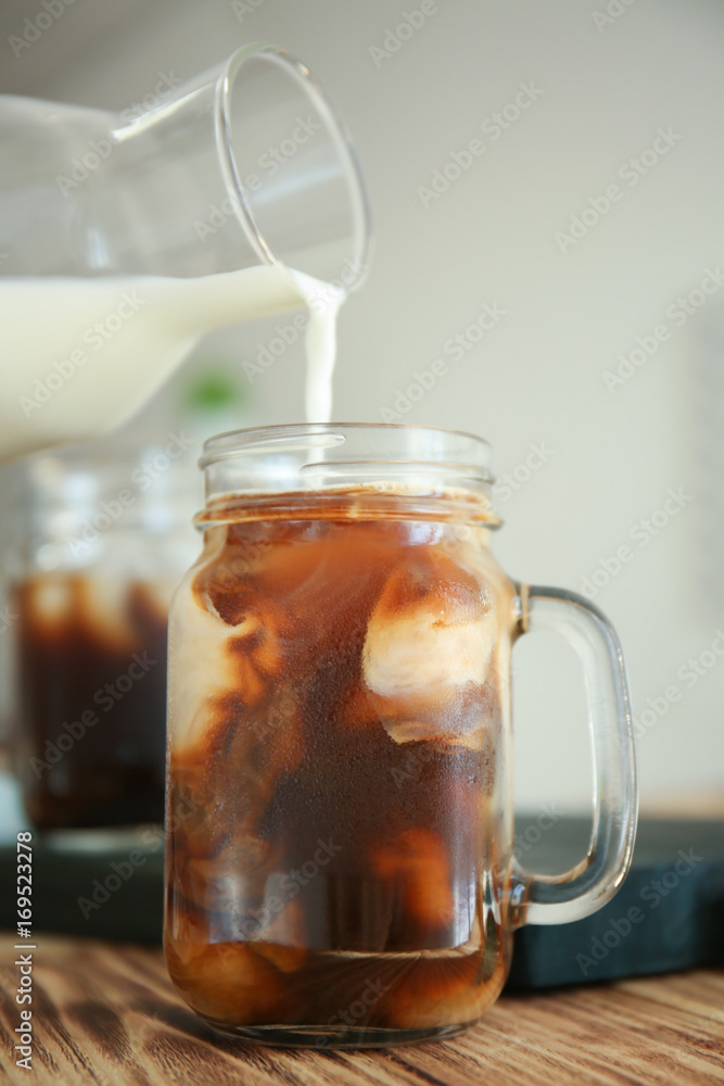 Pouring milk into mason jar with cold brew coffee on wooden table Pouring milk into mason jar with cold brew coffee on wooden table