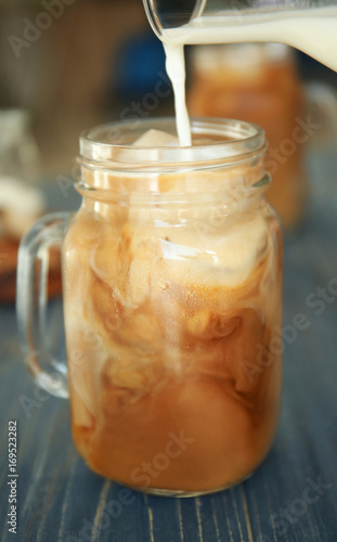 Pouring milk into mason jar with cold brew coffee on wooden table