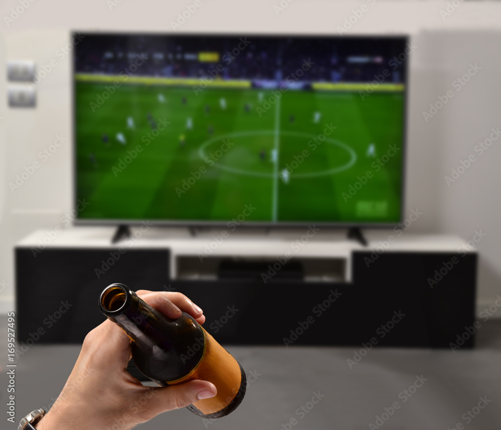 Viendo el partido de futbol en la tv con mi cerveza. foto de Stock | Adobe