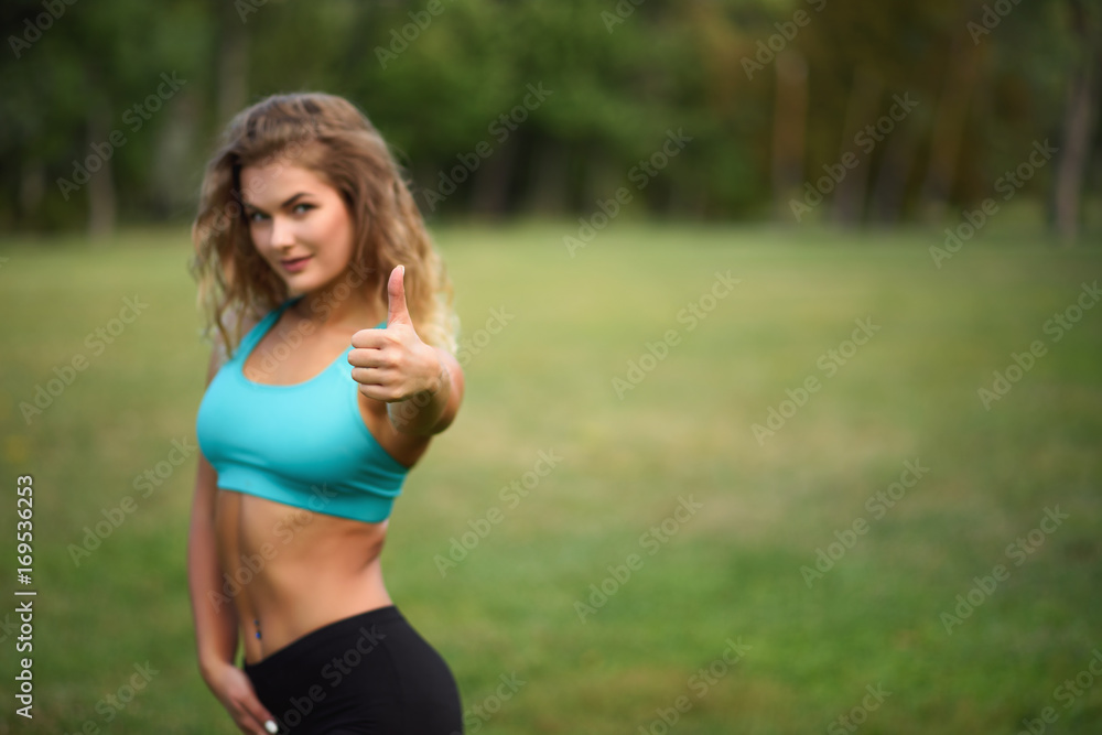 Happy young woman giving a thumbs up in the park. Sport body Happy young woman giving a thumbs up in the park. Sport body