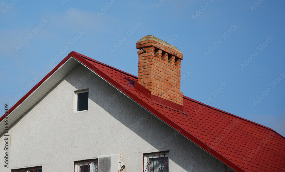 Close up on brick chimney with red metal tile roof. Roofing Construction.