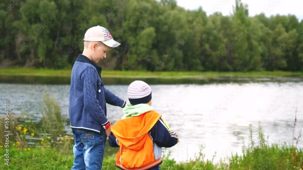Two boys holding hands stand by the river in summer day in slow motion. 3840x2160 Two boys holding hands stand by the river in summer day in slow motion. 3840x2160