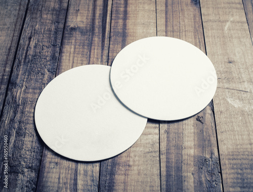 Two blank white beer coasters on vintage wooden table background.