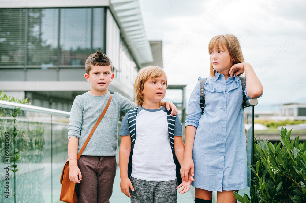 Obraz premium Group of 3 funny schoolkids posing outdoors, wearing backpacks. Back to school concept. Fashion for children