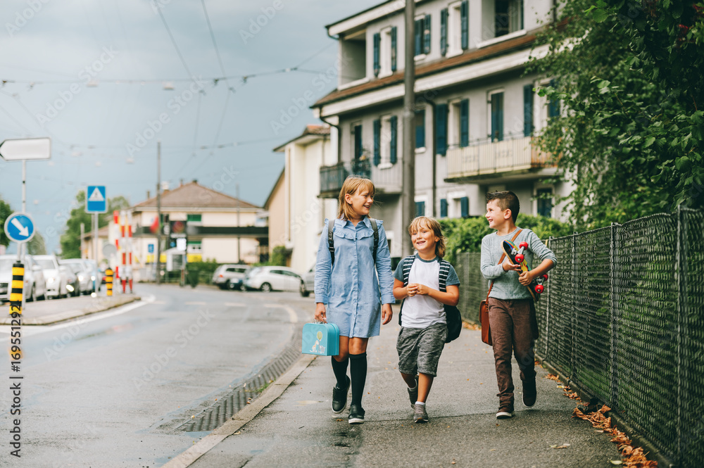 Group of 3 funny schoolkids walking back to school together, wearing backpacks, holding lunch box and skateboard Group of 3 funny schoolkids walking back to school together, wearing backpacks, holding lunch box and skateboard