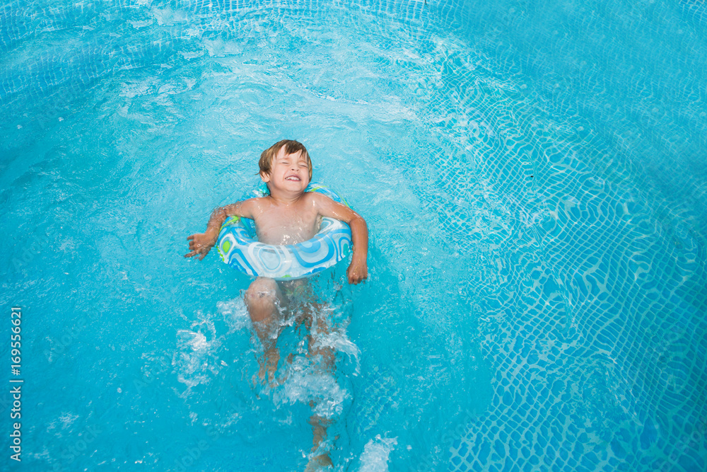 Little boy swimming in the pool with rubber ring, having fun in swimming pool.
