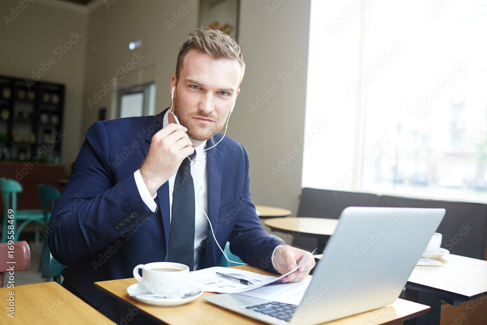 Businessman with earphones and paper working in front of laptop Businessman with earphones and paper working in front of laptop