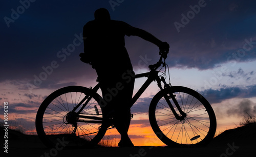 Fototapeta Naklejka Na Ścianę i Meble -  Silhouette of cyclist on the background of sunset. Biker with bicycle on the sand during sunrise