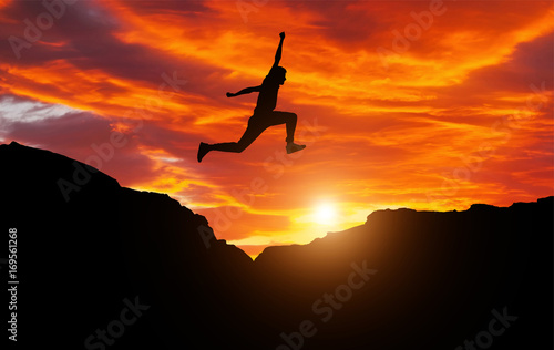 Silhouette of athlete, jumping over rocks in mountain area against sunset. Training running and jumping in difficult conditions in a beautiful nature with cloudy sky photo