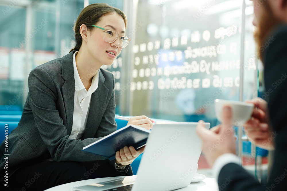 Young woman with notebook talking to colleague at meeting Young woman with notebook talking to colleague at meeting