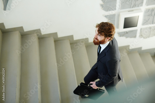 Businessman with briefcase going upstairs on staircase