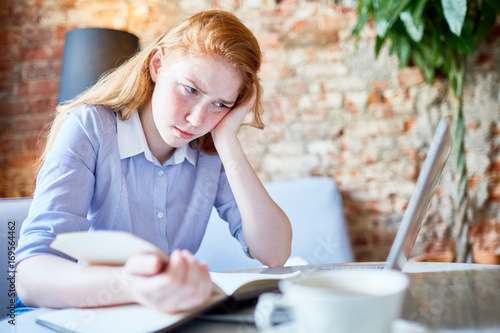 Foto Sulky girl reading book while preparing homework