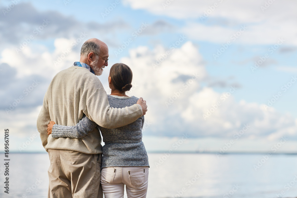 Obraz premium Embracing seniors having talk by seaside during vacation on summer resort