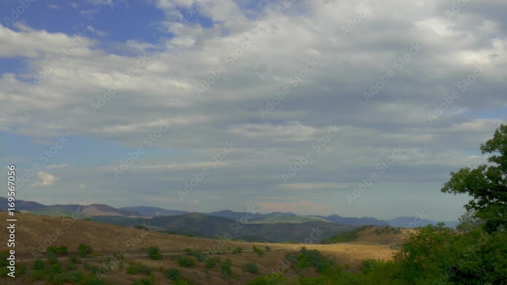Suburban highway through hilly terrain / Road through hilly terrain on background of blue mountains and gray clouds Suburban highway through hilly terrain / Road through hilly terrain on background of blue mountains and gray clouds