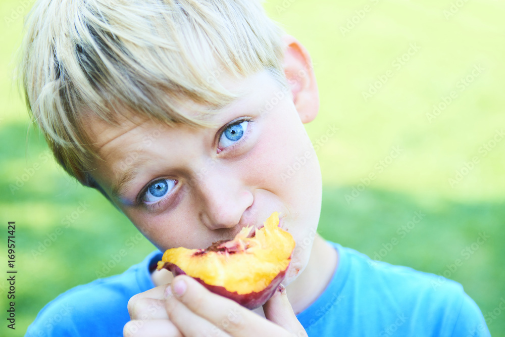 Portrait of child boy eating peach. Happy child in sun summer day. Kid with fruit in nature background. Portrait of child boy eating peach. Happy child in sun summer day. Kid with fruit in nature background.