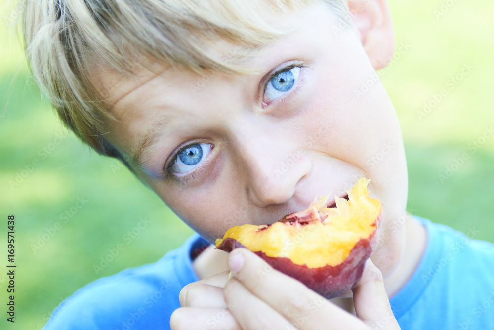 Portrait of child boy eating peach. Happy child in sun summer day. Kid with fruit in nature background. Portrait of child boy eating peach. Happy child in sun summer day. Kid with fruit in nature background.