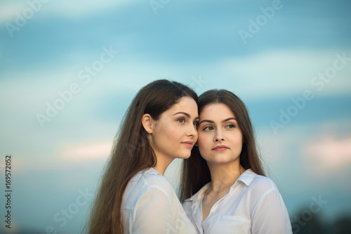 Two beautiful young girl sisters twins on blue sky background